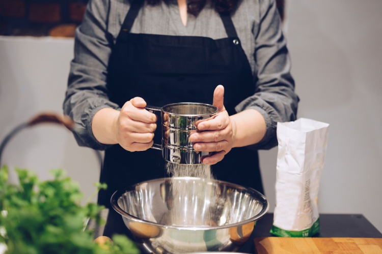 A female cook sifting white flour into a bowl to make pastry